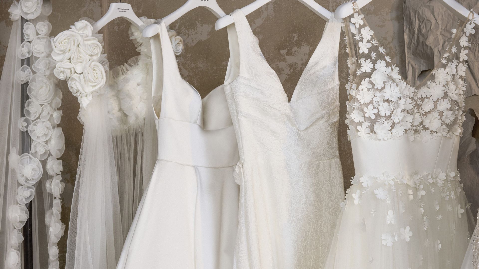 Justin Alexander wedding dresses featuring floral lace, clean satin, and textured bridal details displayed on hangers.